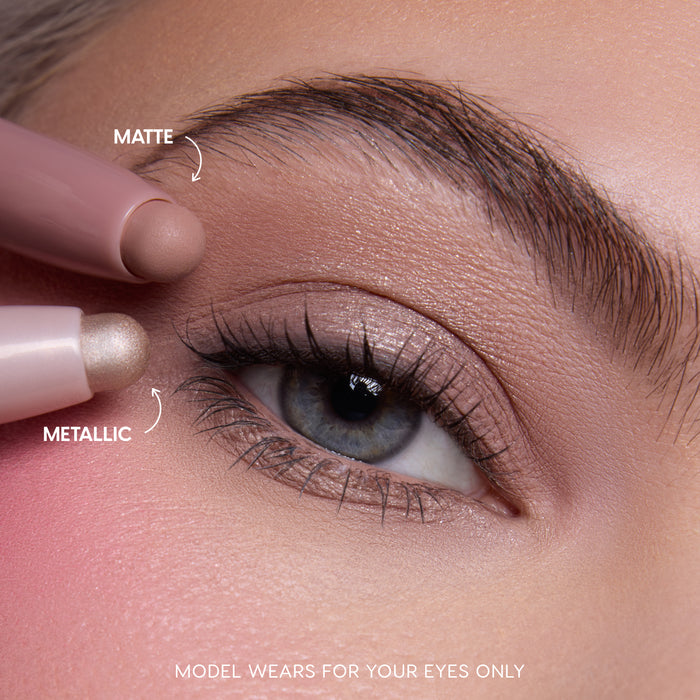 Close-up of a fair-skinned model’s blue eye wearing shimmery neutral shadow created with the All Eyes On Me Heart to Get Shadow Stix Set, showing matte and metallic cream eyeshadow tips applying blendable color on the eyelid.