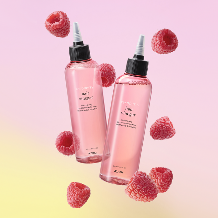 Two pink bottle labeled 'hair vinegar' with a black cap and white text, branded as A'pieu. With raspberries around them.