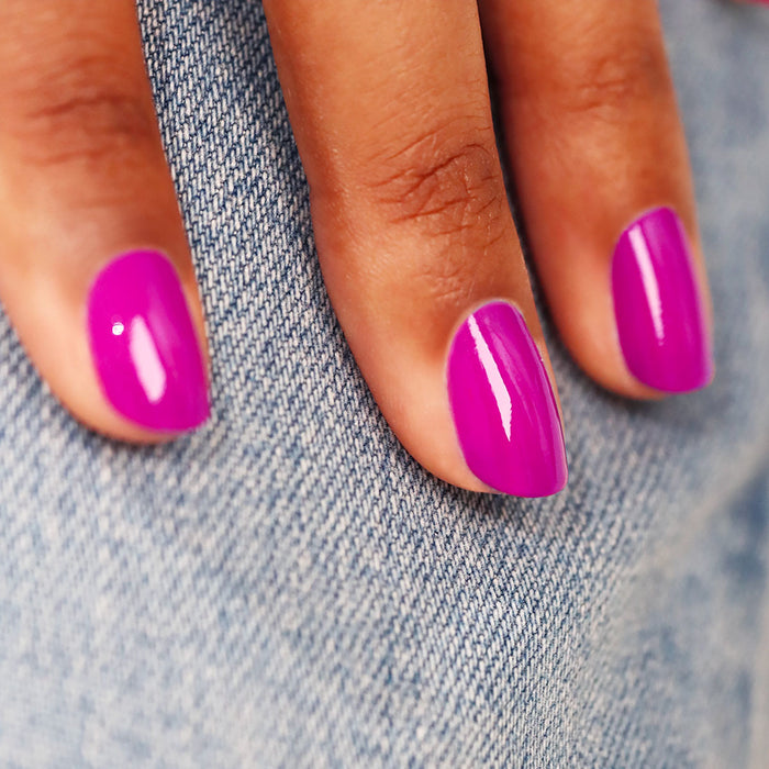 A close-up of a hand with Manucurist's Armeria gel polish—a vibrant mauve shade—resting on blue denim fabric.