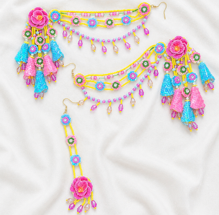 A colorful beaded jewelry set laid flat on a white fabric background, including a waist chain, matching necklace, dangling earring, and decorative tassel pieces in pink, blue, yellow, green, and purple.