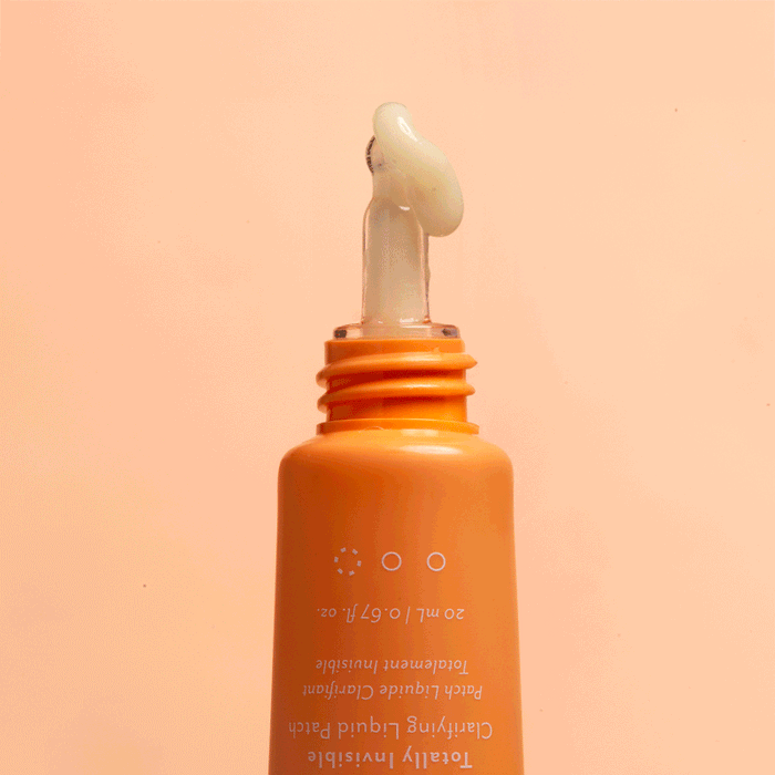 Close-up of orange Patchology tube with applicator tip dispensing a swirl of translucent gel against a peach background