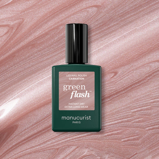 A bottle of Manucurist Carnation Green Flash gel polish is displayed on a pearly pink, shimmery marbled surface resembling nail polish.