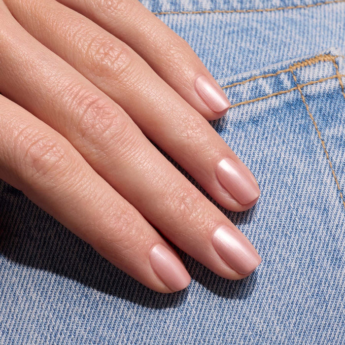 A hand with neatly manicured nails painted in Manucurist's Carnation gel polish rests on light blue denim fabric.