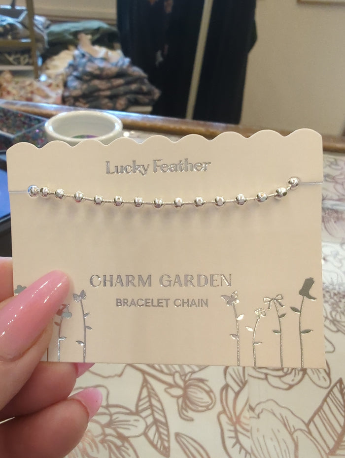 Silver charm bracelet chain by Lucky Feather featuring delicate links and intricate charm details.