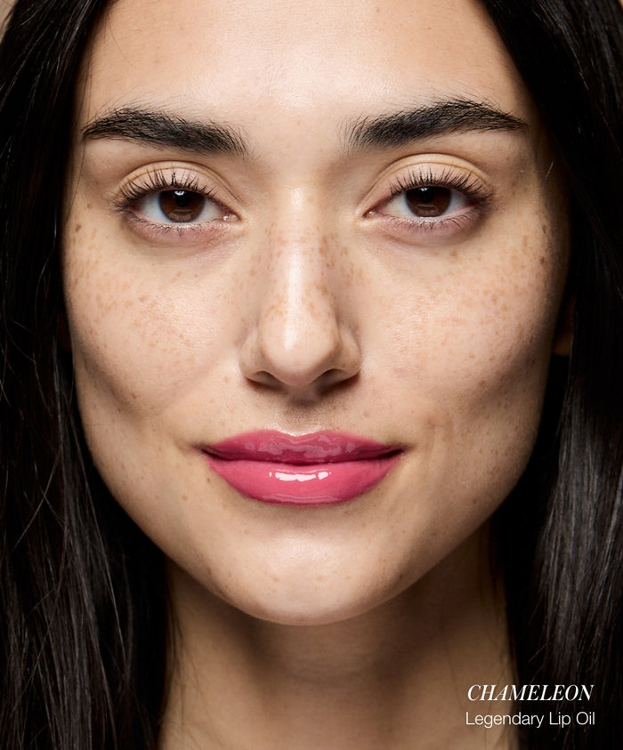 Close-up of a woman with natural freckles wearing glossy pink lip color labeled Color Capsule: Strawberry Matcha, showcasing clean beauty and sustainable packaging.