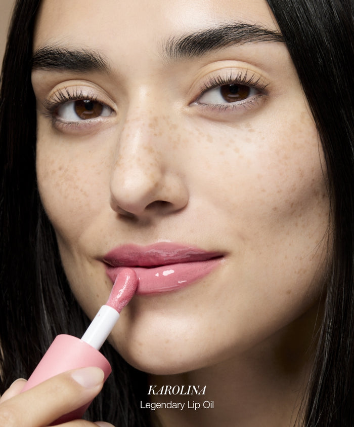 Close-up of a woman applying pink lip oil with a soft applicator, showcasing smooth, natural lips and radiant skin, highlighting Color Capsule: The Rosé Edit.