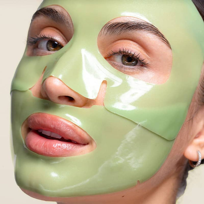 A woman wearing a green cool crush hydrogel face mask on a plain background