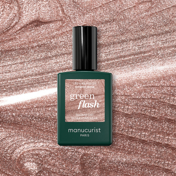 A bottle of Manucurist Cosmic Rose nail polish sits on a sparkling, rose-pink background that perfectly complements the iridescent pink shade.