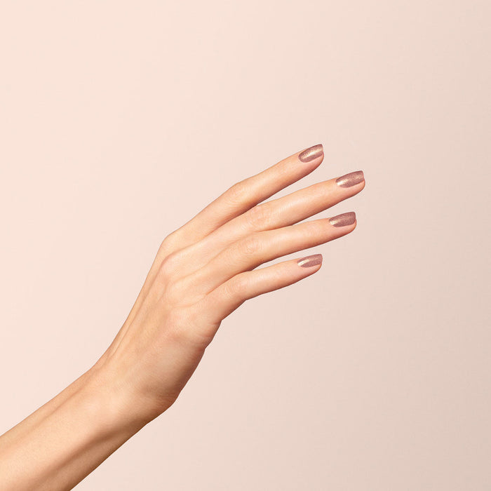 A close-up of a hand with slender fingers and neatly manicured nails painted in Manucurist's Cosmic Rose, an iridescent pink polish, posed gracefully against a soft beige background.