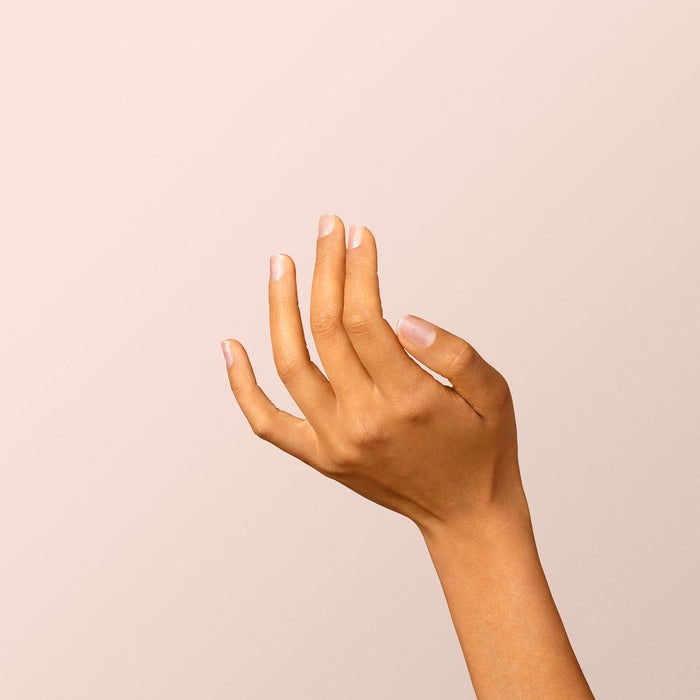 A hand with light brown skin and neatly trimmed nails painted with Manucurist's Diamant shiny silver gel polish is held up against a plain beige background, fingers gently curved.
