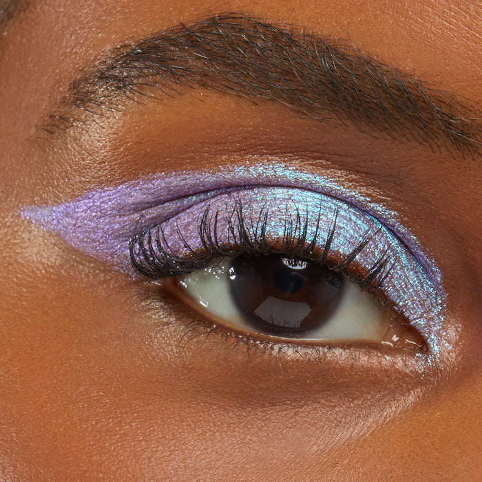 Close-up of an eye wearing Colourpop Disco Disco Shadow Stix, showcasing metallic lavender and icy blue shimmer layered across the lid and winged outwards against smooth medium-brown skin, highlighting bold, multidimensional eye makeup.