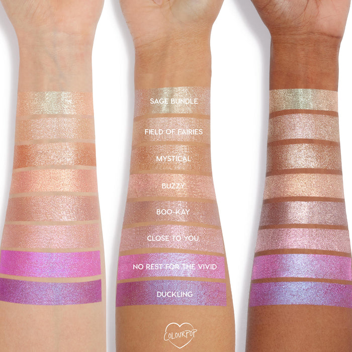 ColourPop Jelly Much Shadow in Duckling swatched in wide stripes on three skin tones, showing a metallic lavender-purple hue with blue iridescent shift; studio arm swatch lineup highlights pigment, shimmer, and payoff.