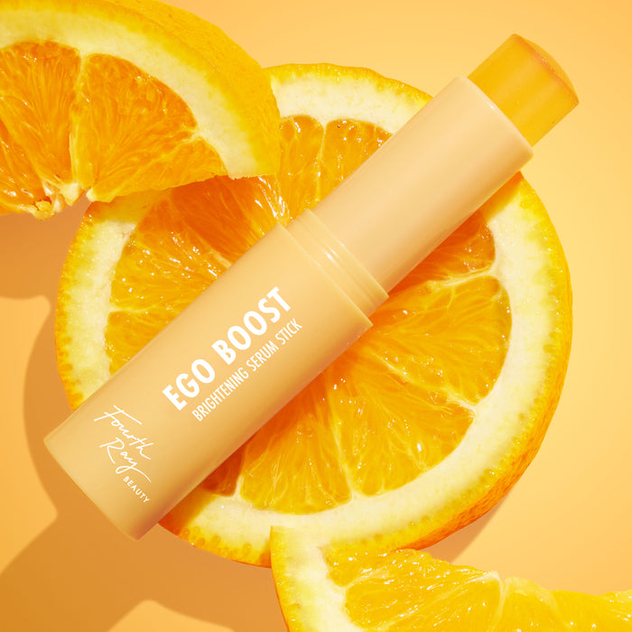 Ego Boost Brightening Serum Stick by Fourth Ray Beauty, a ColourPop Serum Stick, shown uncapped with the peach tube angled across juicy orange slices on a warm citrus backdrop, highlighting its twist-up balm and sunny vitamin C–inspired glow.