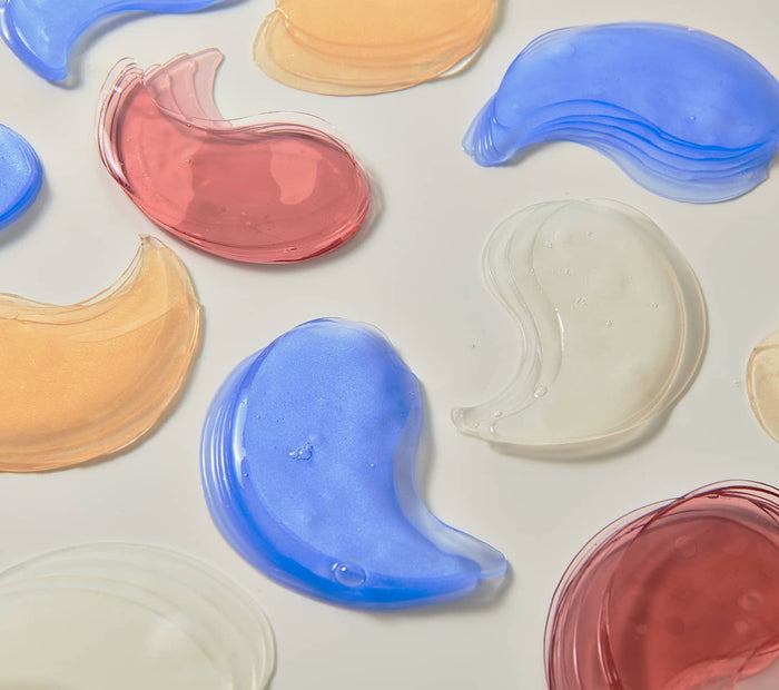 Colorful hydrogel eye patches in blue, pink, gold, and clear tones arranged on a clean surface for skincare use