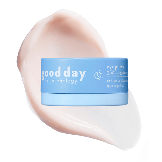 A light blue cosmetic jar labeled 'good day eye pillow 360° brightening' centered over a large pale pink cream smear on a solid green background.