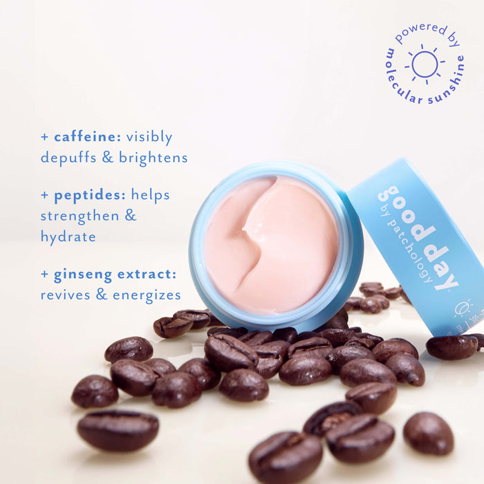 A cosmetic cream jar with a light blue lid lies on its side on a white background, surrounded by scattered coffee beans. The cream inside is a pale pink.