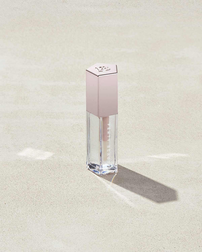 A closed tube of Gloss Bomb Universal Lip Luminizer in the shade Glass Slipper on a grey background.
