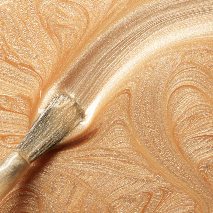 A close-up of a brush spreading Manucurist’s Gold Sand, creating swirling, shimmery patterns with a textured surface reminiscent of iridescent nail polish.