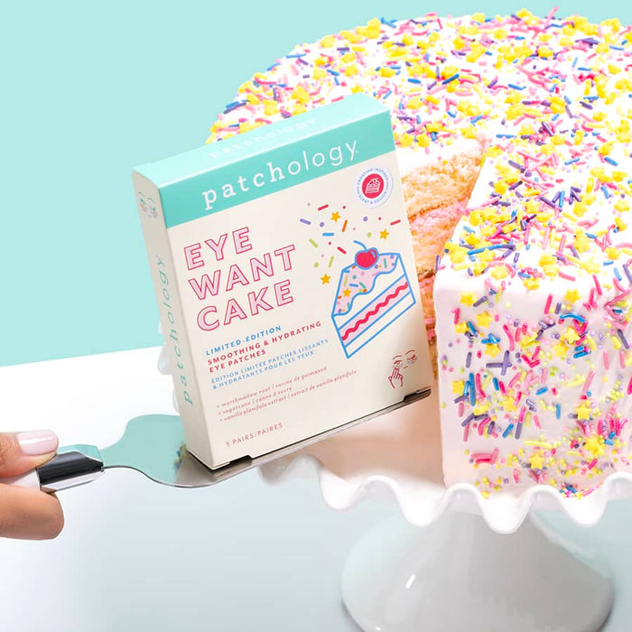 Patchology Eye Want Cake eye patches box beside a sprinkle-covered cake slice on a stand, highlighting a playful, dessert-inspired brightening and hydrating under-eye treatment