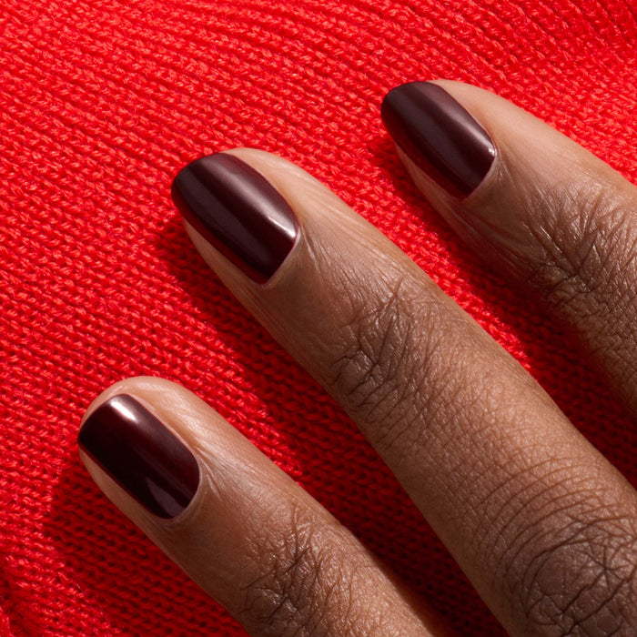 A close-up of a hand with Manucurist Hollyhock gel polish on the nails, resting on textured bright red fabric.