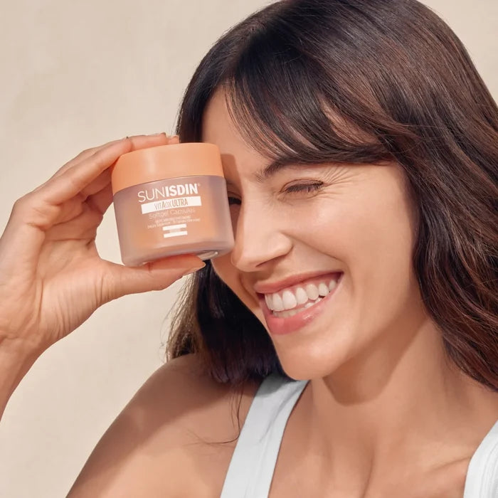 Smiling woman holding ISDIN SUNISDIN vitAox ULTRA softgel capsules jar