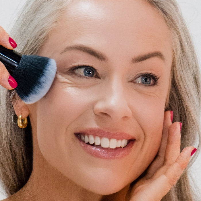 Woman using a Demure Kabuki Brush applying makeup to her face.