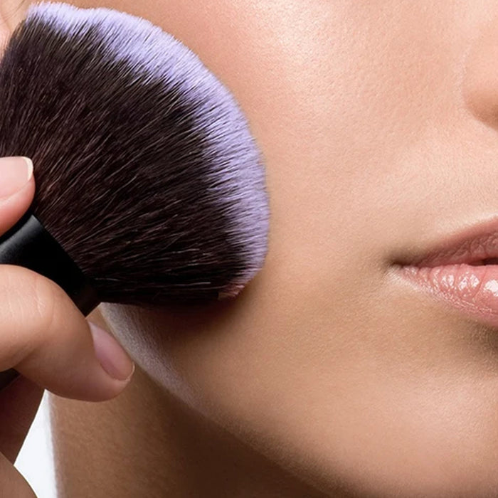 Closeup of Demure Kabuki Brush against a woman's cheek.