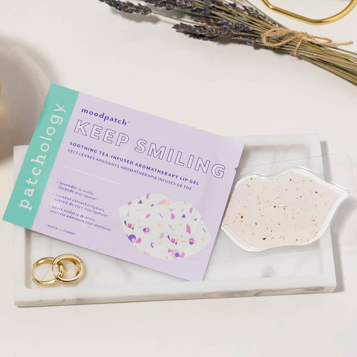 Patchology Keep Smiling lip gel beside a speckled lip mask on a marble tray.