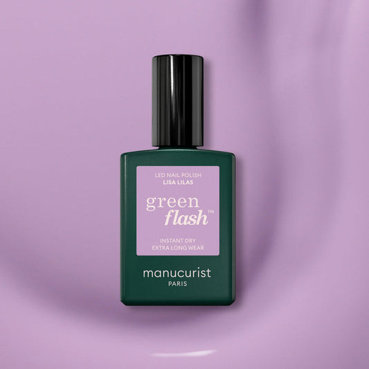 A bottle of Manucurist Lisa Lilas gel polish featuring a dark green base, black cap, and purple label rests on a smooth light purple surface, exuding subtle 90s vibes.