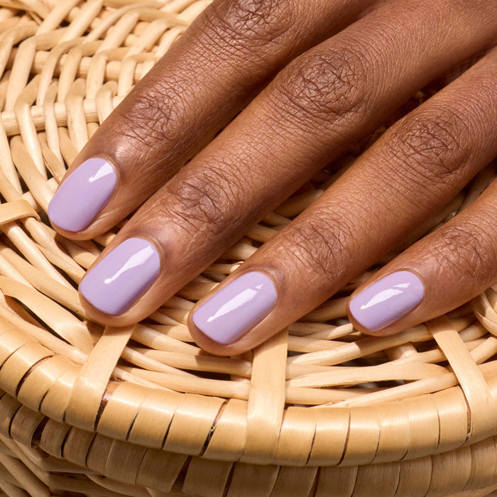 A close-up of a hand with neatly manicured short nails in glossy Lisa Lilas gel polish by Manucurist rests on wicker, evoking subtle 90s vibes.
