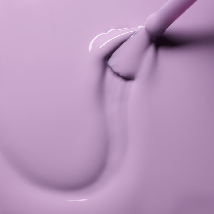 A close-up of Manucurist’s Lisa Lilas brush gliding glossy lilac gel polish in smooth strokes, revealing a shiny, creamy texture with soft reflections and subtle 90s vibes.