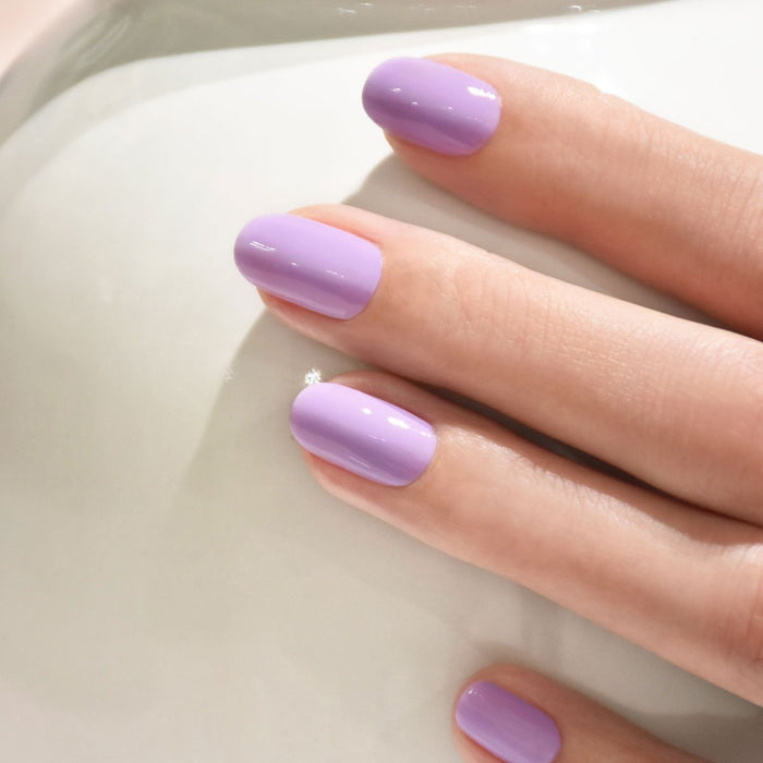 A close-up of a hand with neatly manicured nails painted in Manucurist’s Lisa Lilas gel polish, resting on a smooth white surface for subtle 90s vibes.