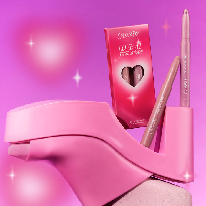 ColourPop Love At First Swipe Shadow Stix from the Heart to Get collection standing upright beside its heart-cutout pink box, styled on a chunky pink high heel against a glowing pink background for a playful makeup product shot.
