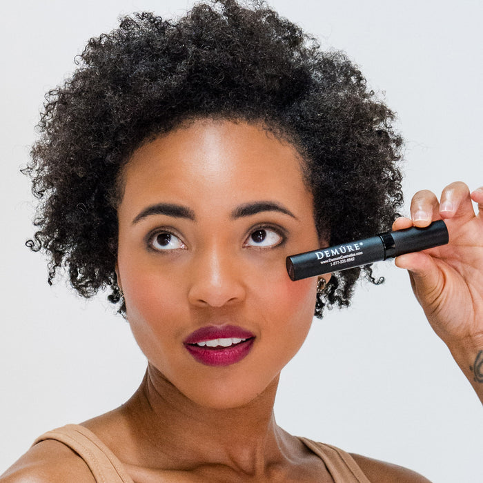 Woman wearing Demure High Def Black Mascara holding a tube near her eye