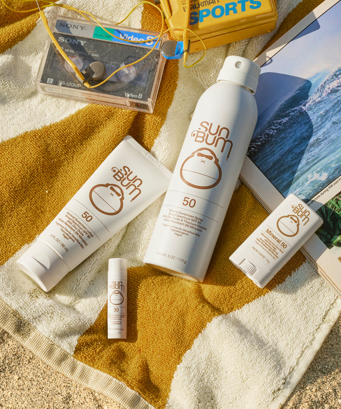 Sun Bum sunscreen products on a towel with a beach scene in the background