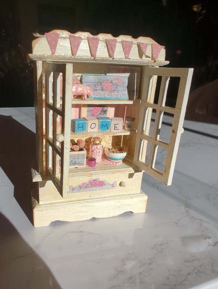 Miniature pink and white hutch scene from Detail In Miniature, featuring tiny furniture and decorative details in a miniature setting.