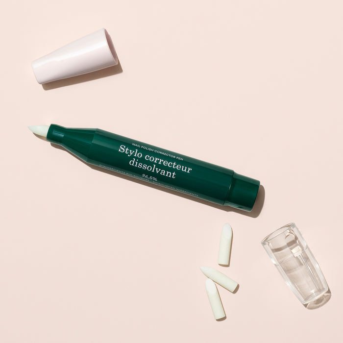 The Manucurist-test + Corrector Pen for gel polish, shown in green without its white cap, includes two spare tips and a small transparent cap, all displayed on a light beige surface.