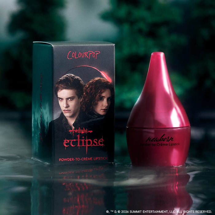 ColourPop Newborn powder to creme lipstick from the Twilight Eclipse collection stands beside its dark forest-themed box with red logo and character art, reflected dramatically on misty water for a moody, cinematic beauty product shot.