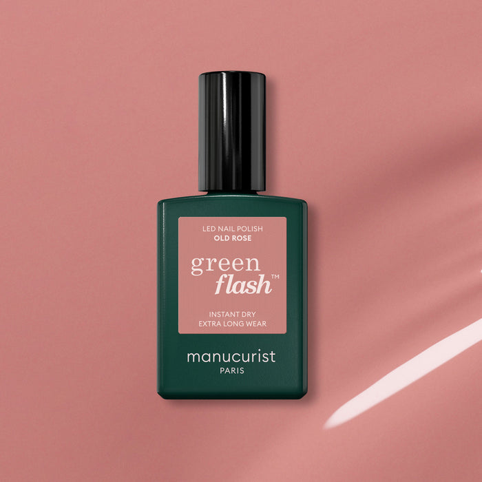 A bottle of Manucurist Old Rose, a beautiful antique pink polish, sits on a pink surface casting a soft shadow. The bottle has a dark green base and black cap.