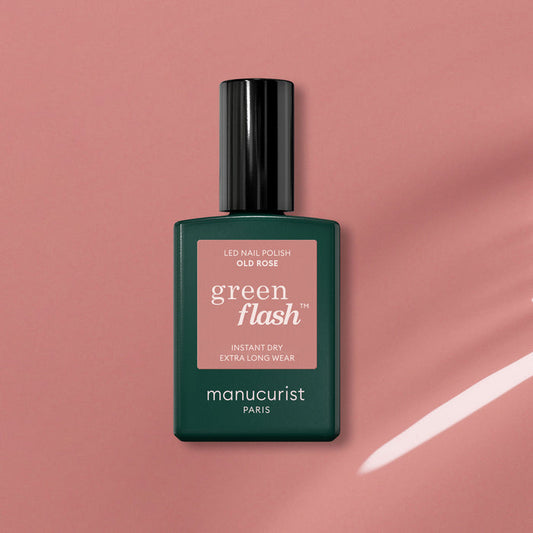 A bottle of Manucurist Old Rose, a beautiful antique pink polish, sits on a pink surface casting a soft shadow. The bottle has a dark green base and black cap.