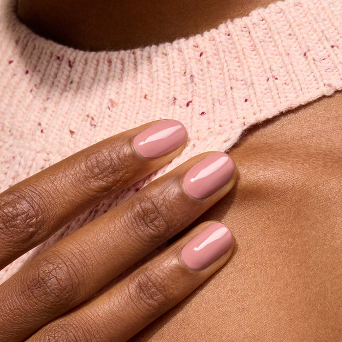 A close-up of a hand with short, neatly manicured nails painted in Manucurist's Old Rose, a glossy antique pink polish, resting on a light pink knitted sweater.