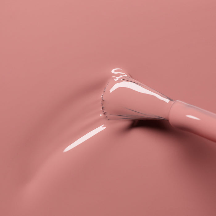 A close-up of a nail polish brush coated in Manucurist’s glossy Old Rose shade, with the smooth antique pink polish spreading across a matching surface.