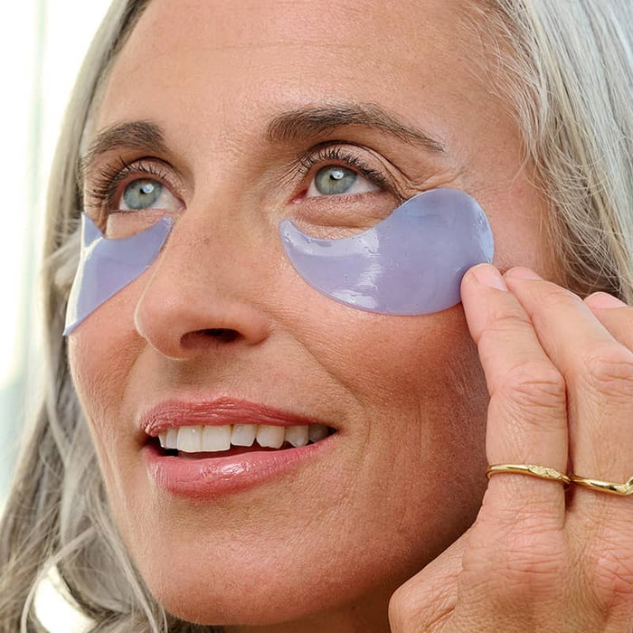 Mature woman applying lavender Patchology Restoring Night Eye Gels for a soothing, overnight undereye treatment.