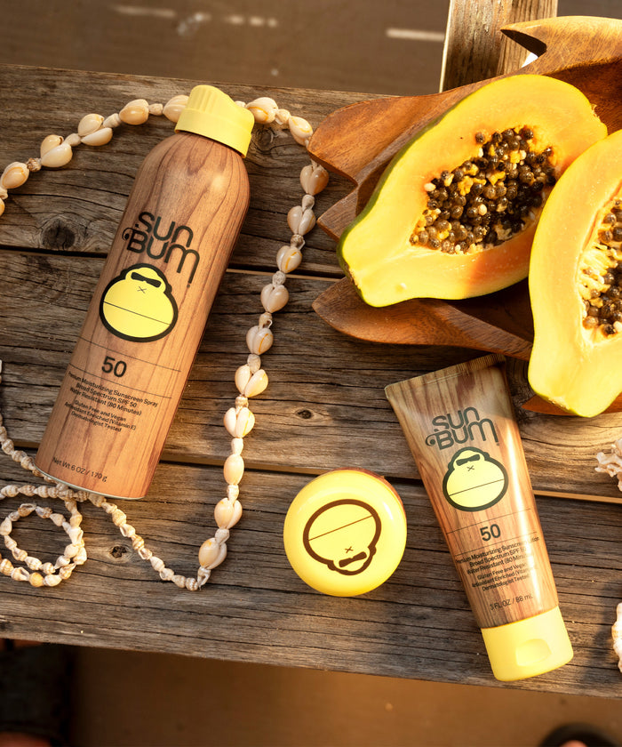 Sun Bum Original SPF 50 Face Cream with tropical papaya and shell necklace on wooden surface.