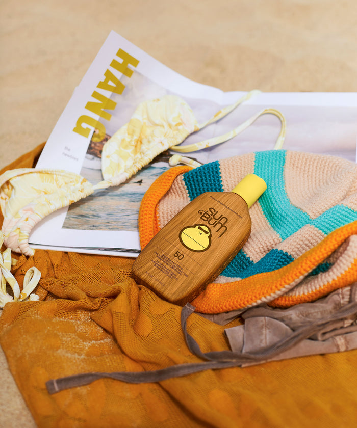 Bottle of Original SPF 50 Sunscreen Lotion placed on beach accessories and a magazine, Sun Bum
