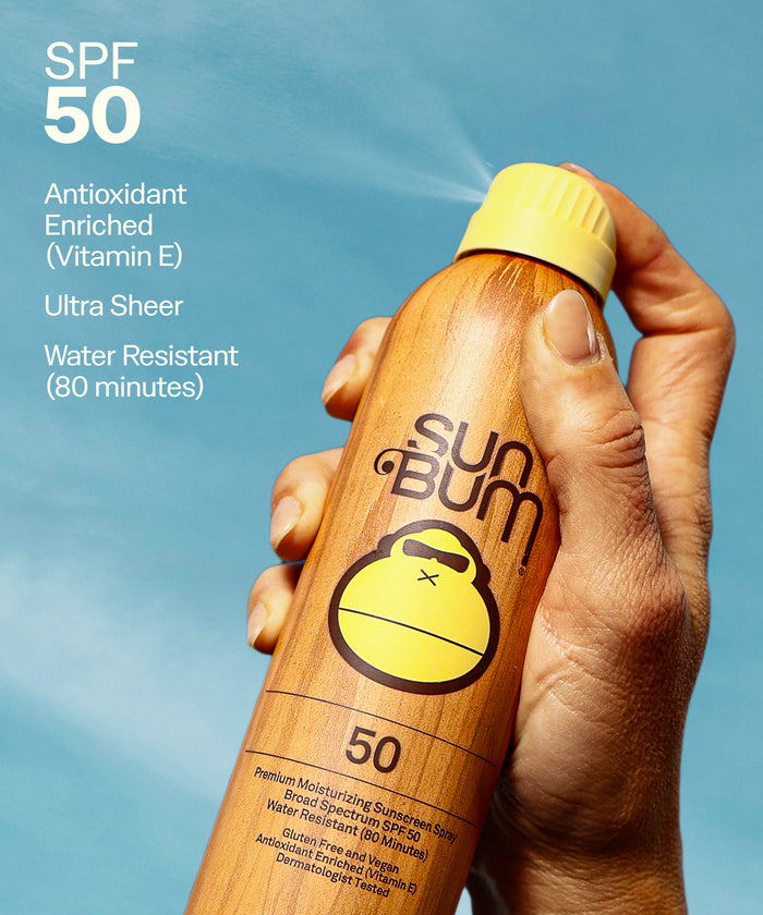 Hand holding a Sun Bum sunscreen bottle with SPF 50 on a blue background