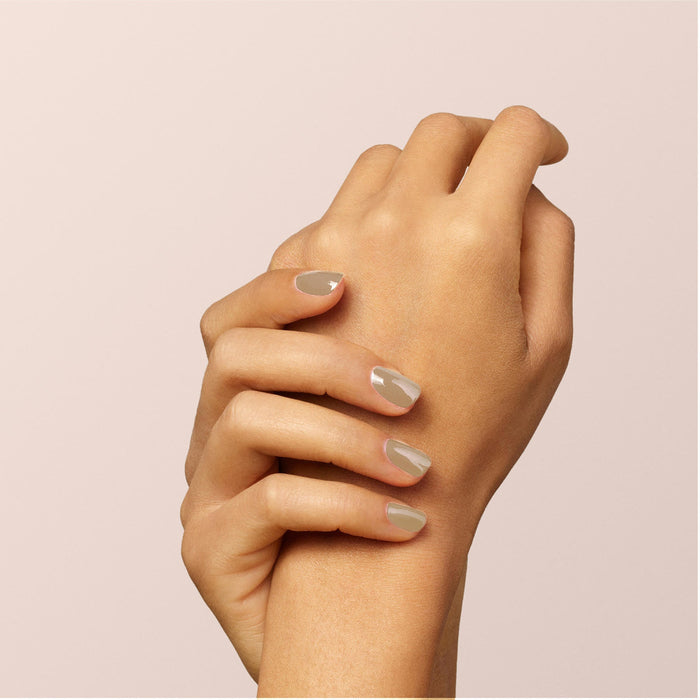 A close-up of two hands with neatly manicured nails painted in Manucurist's Orme, a glossy café au lait nail polish, against a soft beige background.
