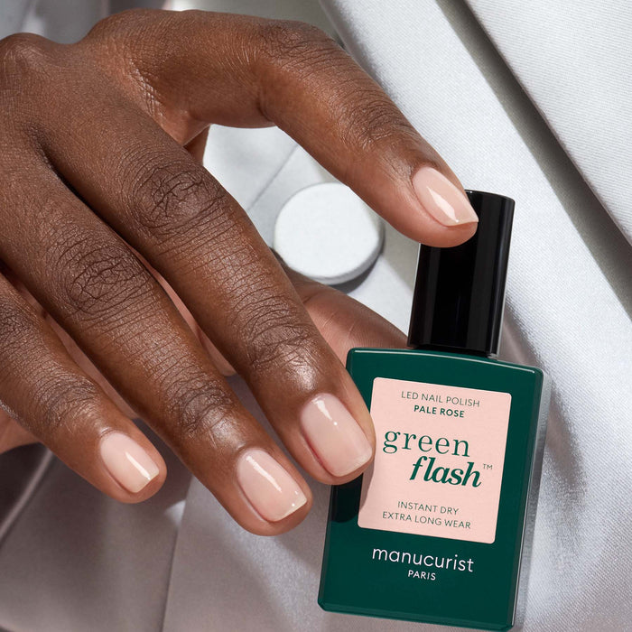 A hand with neatly manicured nails painted in Manucurist’s Pale Rose holds a bottle of the Pale Rose gel polish against a soft, light background.