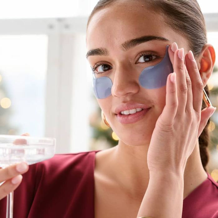 Woman applying eye patches with a blurred indoor background