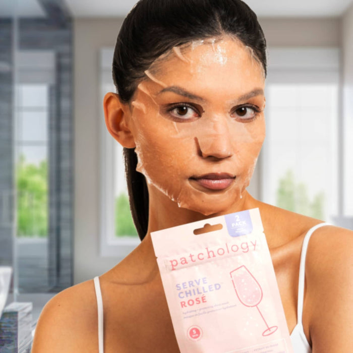 Woman wearing a hydrating sheet mask while holding Patchology Serve Chilled Rosé mask packaging, highlighting a refreshing, glow-boosting skincare treatment for radiant skin